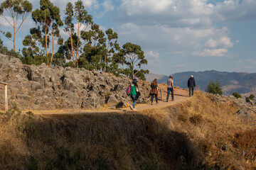 4 turistas caminando por la zona arqueológica de Qenqo en Cusco, Perú, rodeado de árboles de eucalipto