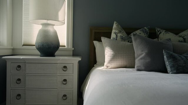 Dimly lit bedroom with nightstand, lamp, and sunlit bed