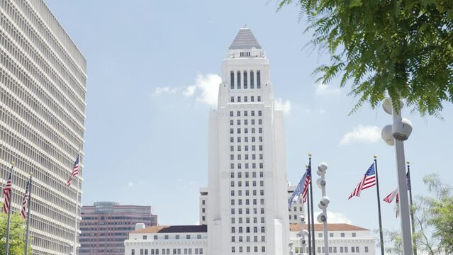 View onto the city hall of Los Angeles near while airplane passing near Clara Shortridge Folz Criminal Justice center of the Gloria Monila Grand Park during summer time american flags in front steady