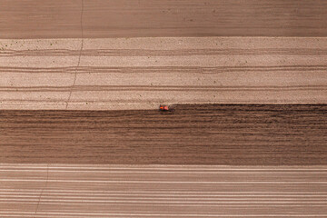 Fototapeta premium Agricultural tractor with tiller attached performing field tillage before the sowing season, aerial shot seen from the drone pov