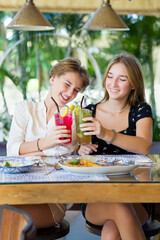 Two happy teenage young girls met each other in the cafe drinking fruit cocktails. Summer warm day on vacations.
