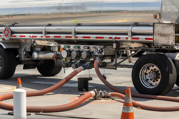 Gasoline being offloaded from a tanker truck into an underground storage tank at a gas station - obrazy, fototapety, plakaty