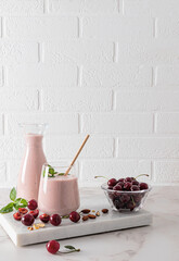 Freshly made homemade cherry smoothie in a bottle and a large glass on a stone board podium with berries and mint leaves. Detox