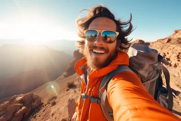 Fotobehang Cappuccino Happy young man hiker taking selfie on top of mountain, smiling tourist with backpack and glasses enjoying beautiful sunset from the top of mountain