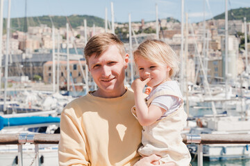 Fototapeta na wymiar A man holds his little daughter in his arms against the yachts, smile