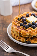 Syrup dripping on Belgian waffle with blueberries for breakfast