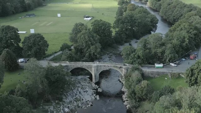 An aerial view of the Devil's Bridge at Kirkby Lonsdale on a summer evening, Yorkshire, England, UK. Flying right to left around the southerly side of the bridge while zooming out.