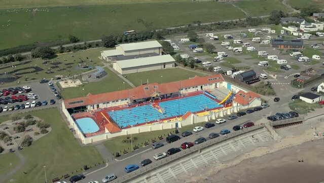 An aerial view of Stonehaven outdoor swimming pool on a sunny summer afternoon, Aberdeenshire, Scotland, UK. Flying left to right around the pool while zooming out.