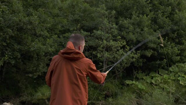 Slow motion shot of a fisherman flyfishing and casting his line into the river