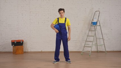 Full length shot of a smiling young construction worker standing in the room under renovation,...
