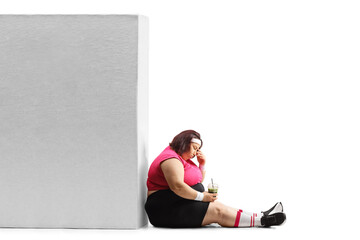 Sad overweight woman in sportswear holding a healthy green shake and sitting on the ground