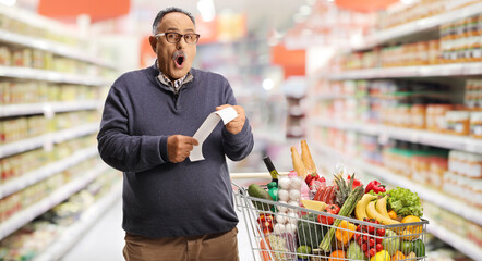 Surprised mature man with a shopping cart holding a bill
