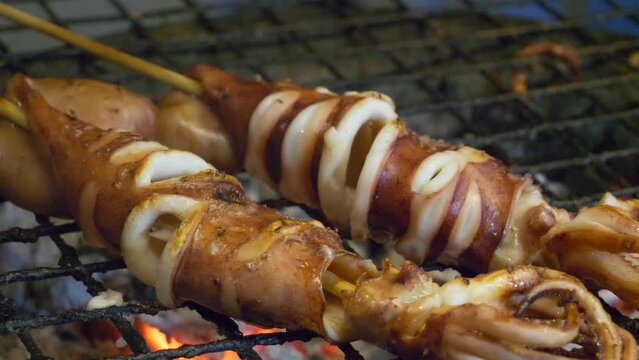 thailand night market street food booth squid in stick grill cooked juicy on hot charcoal