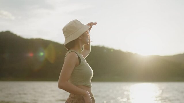 Footage of a woman walking by the lake and mountain in evening with golden sunset. Travel to nature place.