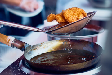 Fried meat in breadcrumbs in a colander in a wok pan with boiling oil. Cooking Chinese food up close. Fat drips into the pan. Asian chef at work.