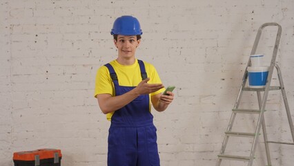 Medium shot of a young construction worker standing in the room, holding a smartphone, typing, searching, chatting, reacting with astonishment.