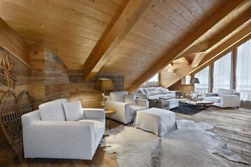 modern sofa and armchairs made of fabric in the living room in the rustic attic with wooden floor and wooden wainscoting