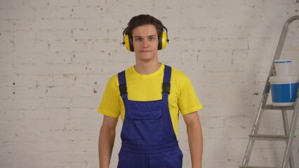 Medium shot of a construction worker standing in the room under renovation, wearing a earmuffs, noise cancelling headphones and smiling.