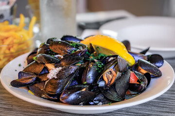 Freshly cooked mussels steamed in white wine sauce or moules marinieres on a plate at a restaurant in Menton Old Town, French Riviera, South of France - obrazy, fototapety, plakaty