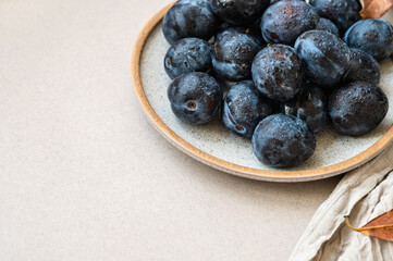Fresh plums with water drops on plate, on neutral beige background with copy space