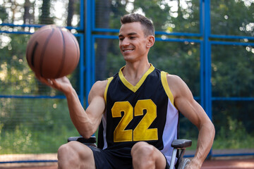 Fototapeta premium Young man in wheelchair playing basketball outdoor.