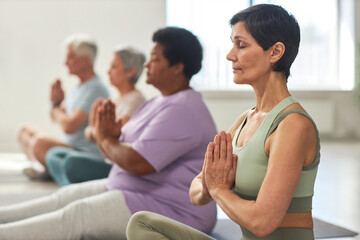 Group of people sitting in lotus position and meditating in yoga class - Powered by Adobe
