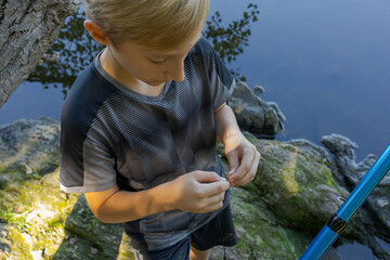 The teen angler checks the bait and puts a new one on. Sport fishing on the river in summer.