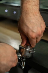 Close-up of barista holding portafilter and coffee tamper making an espresso coffee in cafe or coffee shop.
