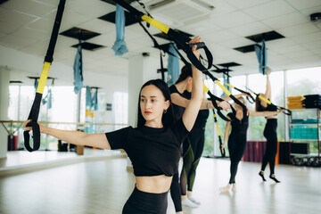 Group of active sports girls in black sportswear are engaged in budgie fitness in the gym. Bungee...