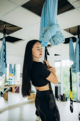 Beautiful female gymnast doing stretching on fabric hangers in a spacious hall during training. The concept of a flexible body and healthy joints. Variation of eka pada chakrasana pose, flying yoga