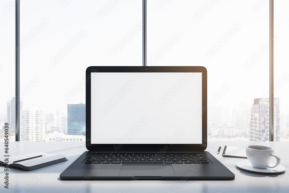 Poster Close up of laptop with empty white mock up monitor, coffee cup and notepad placed on desk. Window with bright city view in the background. 3D Rendering.