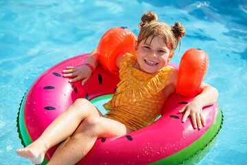 Happy little girl with inflatable toy ring float in swimming pool. Little preschool child learning...