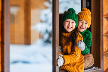 Hello winter holiday! Happy children play together outdoor in open window. Happy New Year and Merry...