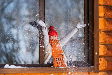 Hello winter holiday! Happy child play with snow outdoor in open window. Happy New Year and Merry Christmas family celebration!