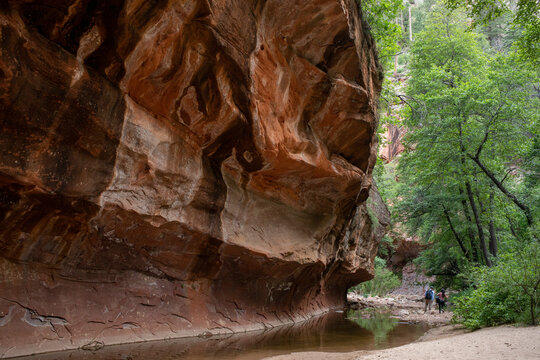 Hikers walking away near stream under rock ledge