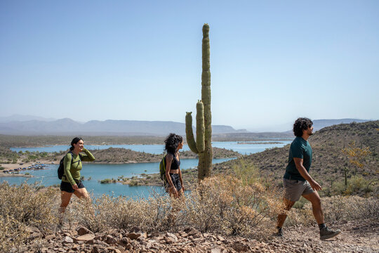 Hikers pass saguaro cactus on desert mountain trail by lake