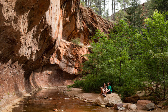 Young couple sit on rock by stream under rock ledge