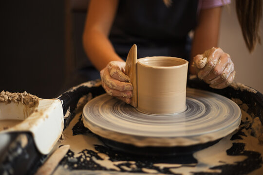 Close up of teenage girl's hands molds clay pot spinning on pott
