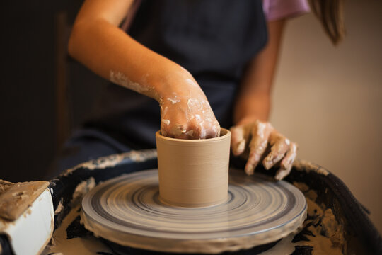 Close up of teenage girl's molds clay pot spinning on pottery wh