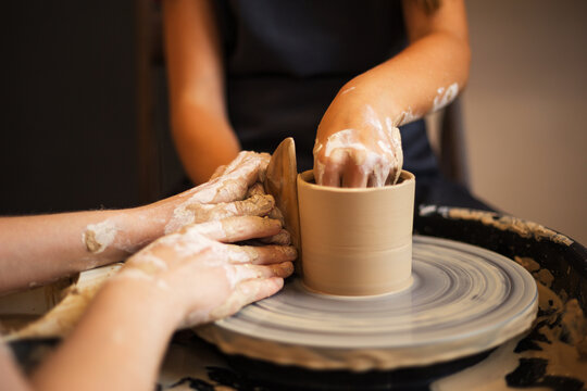 Hands of a young girl and a child creating cup on a Potter's whe