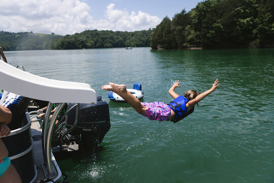 Child sliding off pontoon boat slide into lake on belly