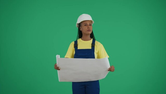 Medium green screen isolated chroma key video of a dark-skinned young female construction worker studying and comparing her plan to the surroundings.