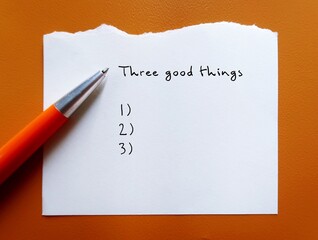 Pen on orange background with handwritten text Three good things - gratitude practice journal to...