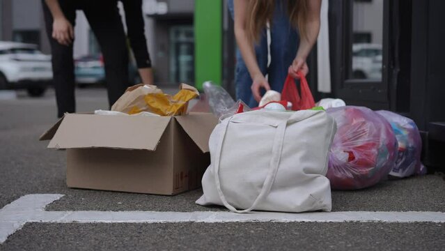 Close-up Garbage Bags With Unrecognizable Young Couple Sorting Trash Outdoors. Young Caucasian Man And Woman Throwing Away Litter Separating Rubbish