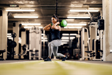 A female bodybuilder is doing lunges with heavy weights on her shoulders in a gym.
