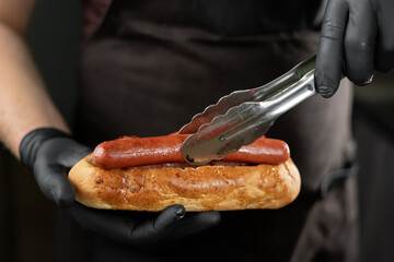 Male in gloves putting sausage on a hot dog. Hot dog cooking concept. Creating classic fast food.