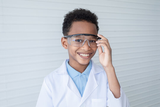Portrait of African schoolboy in lab coat uniform wearing safety eyeglasses smile looking at camera on white background, dreaming of elementary student boy to be scientist or specialist doctor concept