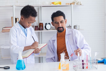 Hispanic or Indian teacher wearing lab coat teaching African elementary students boy kid writing report in laboratory science class, lifestyle modern education at school for national pupil concept