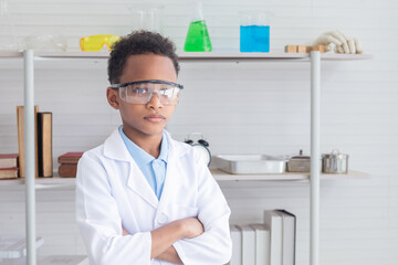 Portrait of African student in lab coat uniform arm crossed wearing safety eyeglass in laboratory, cute boy in science classroom, primary school pupil kid scientist or specialist doctor career concept