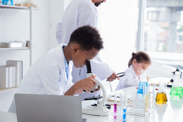 Group of multicultural African boy and elementary students girl kids friend wearing lab coat uniforms using microscope with teacher in laboratory room, lifestyle learning education in science class